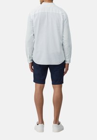 Lichtblauwe overhemd met lange mouwen en een knoopsluiting, gecombineerd met donkerblauwe shorts. Witte sneakers maken de outfit compleet. Gladde stofstructuur.