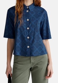 Camicia a maniche corte blu navy con un motivo a diamante testurizzato, dotata di colletto a punta e cinque bottoni di chiusura sul davanti.