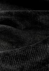 Schwarzer Cordstoff mit gerippter Textur, der weiche, erhabene Linien zeigt, die ein wellenförmiges Muster über die Oberfläche schaffen.