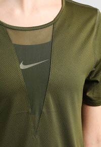 Zbliżenie zielonej siatkowej koszulki sportowej nałożonej na zieloną bluzę Nike z widocznym białym logo w kształcie łyżwy przez dekolt w kształcie litery V.