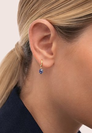 Pendiente de aro dorado con colgante de piedra preciosa azul. El pendiente tiene una superficie lisa y un diseño sencillo que resalta el color de la piedra.