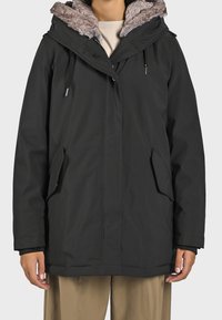 Svart parkasjacka med en texturerad fuskpälsmössa, dragsko, två sidofickor och en rak skärning med en slät finish.