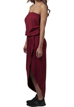 Bordowa sukienka maxi bez ramiączek z elastycznym dekoltem, lejąca się tkanina i rozcięcie z boku. Zestawiona z czarnymi butami sportowymi.