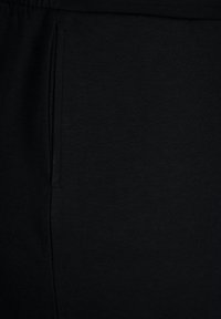 Pantalon en maille noire avec une poche latérale et une taille élastique, présentant une texture lisse et un design simple et minimaliste.