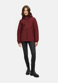 Burgundy hooded jacket with a front zipper, two side pockets, and adjustable drawstrings. Worn over black jeans and chunky black boots.