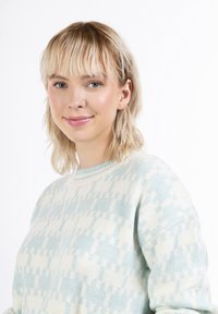 Világoskék és krémszínű pulóver geometriai mintázattal, puha textúrával, kerek nyakkal és hosszú ujjal. A modellen vállig érő haja van.