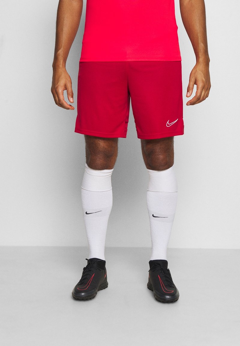 Des shorts de sport Nike rouges en tissu lisse et léger. Associés à des chaussettes blanches montantes et des chaussures noires avec des accents rouges.