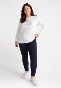 Felpa bianca con un design a contorno floreale e la scritta "È TEMPO DI SBLOOM" abbinata a leggings blu navy con dettagli floreali laterali e sneakers bianche.