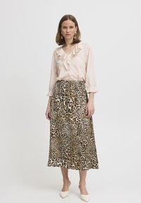 Blusa in seta rosa chiaro con colletto a ruffles; gonna midi leopardata in beige e nero; modella che indossa scarpe bianche a punta.