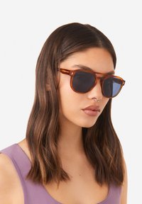 Brýle s tmavými čočkami a kovovými doplňky, ve vzoru želvoviny, s klasickým pravoúhlým tvarem a lesklým povrchem.