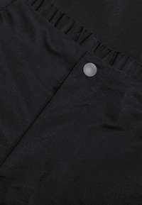 Svart tyg med en subtil lyster, med en gathered-textur längs den övre kanten och en rund grå knapp som ett stängningsdetalj.