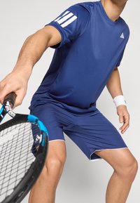 Niebieska sportowa koszulka i szorty wykonane z lekkiego materiału; mają białe paski akcentujące na rękawach oraz białą lamówkę na szortach.