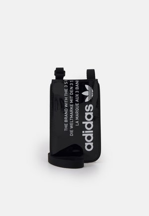Černé lesklé pouzdro Adidas s bílým logem, textem ve třech jazycích a připevněným černým popruhem, stojící vzpřímeně na bílém pozadí.