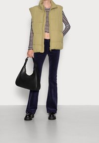 Gilet matelassé vert clair, crop top à carreaux noir et blanc, pantalon évasé bleu foncé, sac à main en cuir noir et chaussures noires chunky.