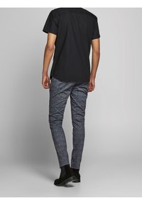 Svart kortärmad skjorta kombinerad med strukturerade blå plaidbyxor och svarta ankelboots, som visar en figursydd passform och ren siluett.