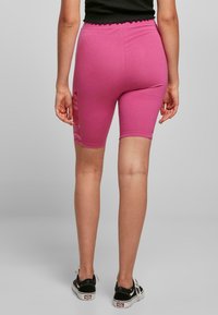 Pantalones cortos de bicicleta de algodón rosa con una cinturilla en forma de ola y detalles de encaje floral en el costado, combinados con zapatos de lona negros.