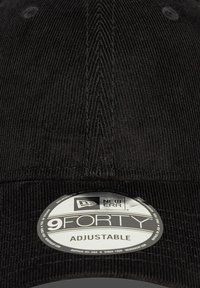 Gorra de pana negra con visera curvada. Presenta una etiqueta de logo circular con la inscripción "9FORTY ADJUSTABLE" de New Era. La textura es acanalada.