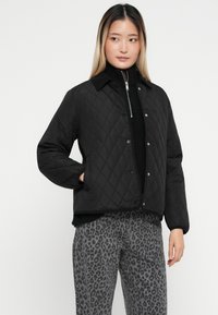 Zwarte gewatteerde jas met een kraag, knoopsluiting aan de voorkant en geribde manchetten, gecombineerd met grijze panterprint broek.