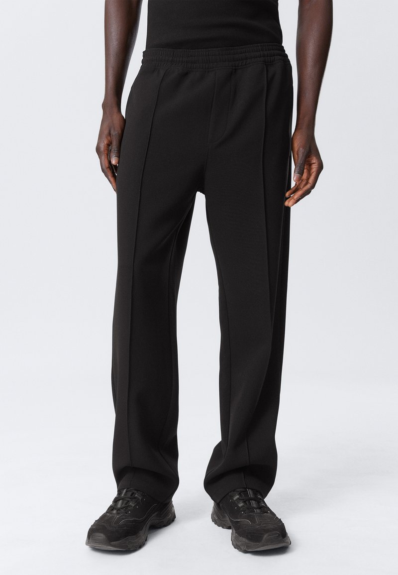 Zwarte sportbroek met een elastische tailleband, met een losse pasvorm en zichtbare naden. Gecombineerd met zwarte sneakers.