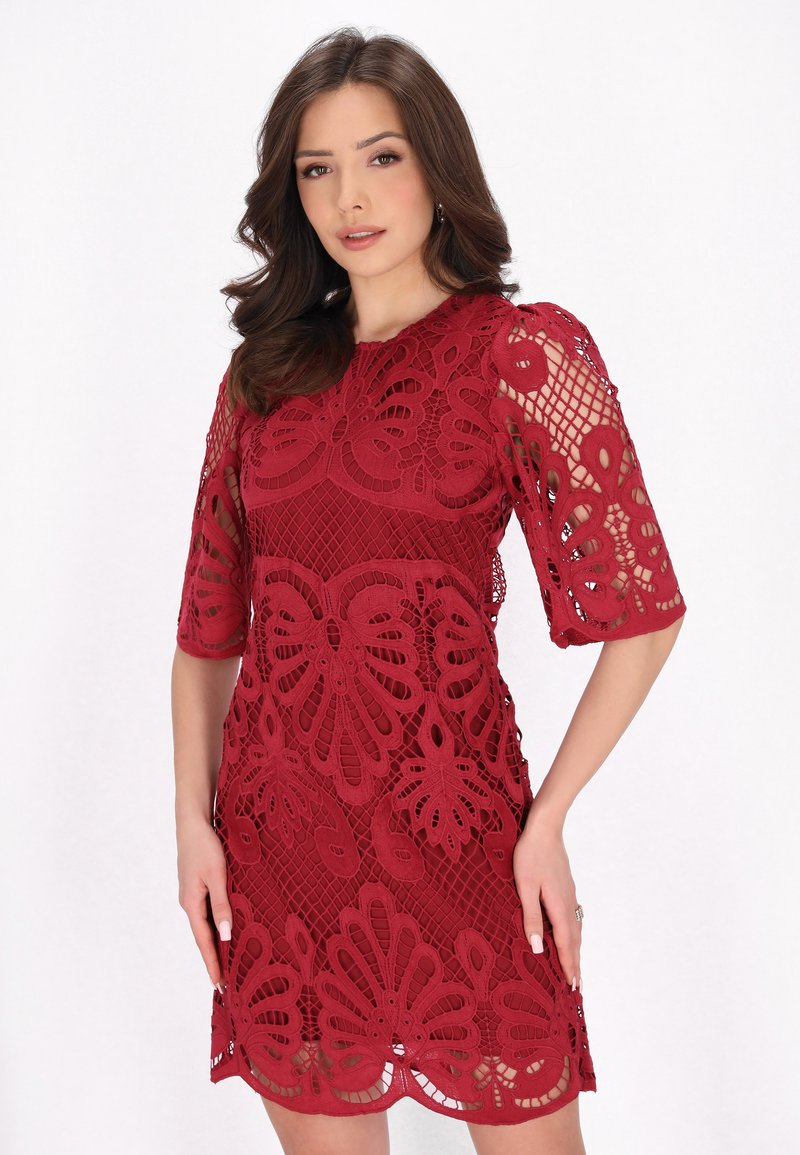 Rotes Spitzenkleid mit floralen Ausschnitten, kurzen Ärmeln und einer taillierten Silhouette, die ein strukturiertes und mehrlagiges Aussehen erzeugt.
