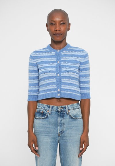 Cardigan court tricoté bleu clair, avec des rayures horizontales, des manches courtes, un col côtelé et une fermeture par boutons. Associé à un jean en denim clair.
