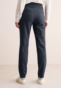 Ciemnoszare dresy wykonane z miękkiego materiału, z luźnym krojem, elastycznym pasem i kieszeniami. Noszone z białymi trampkami.