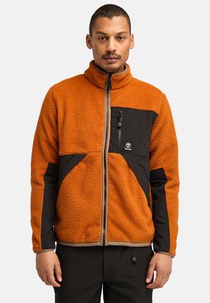 Fleece jacket with an orange body, black fabric accents, a high collar, and a zippered chest pocket. Features a textured exterior.