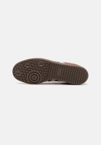 Talpa de cauciuc maro cu un model texturat pentru aderență, accente cu design circular și marcajul "adidas" gravat pe lateral.