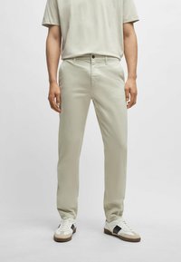 Světlé béžové kalhoty, slim fit, vyrobené z bavlněné směsi, s zipem, předními kapsami a jemnými prošívacími detaily. V kombinaci s bílými teniskami.