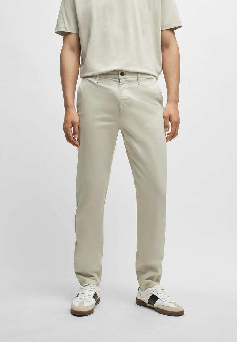 Světlé béžové kalhoty, slim fit, vyrobené z bavlněné směsi, s zipem, předními kapsami a jemnými prošívacími detaily. V kombinaci s bílými teniskami.