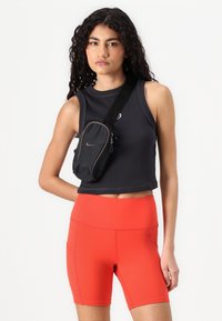 Black sleeveless crop top with ribbed texture, paired with high-waisted red shorts. Small black shoulder bag with zip and logo.