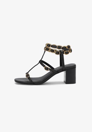 Black leather sandal with an ankle strap featuring gold accents and decorative embellishments, set on a chunky block heel.