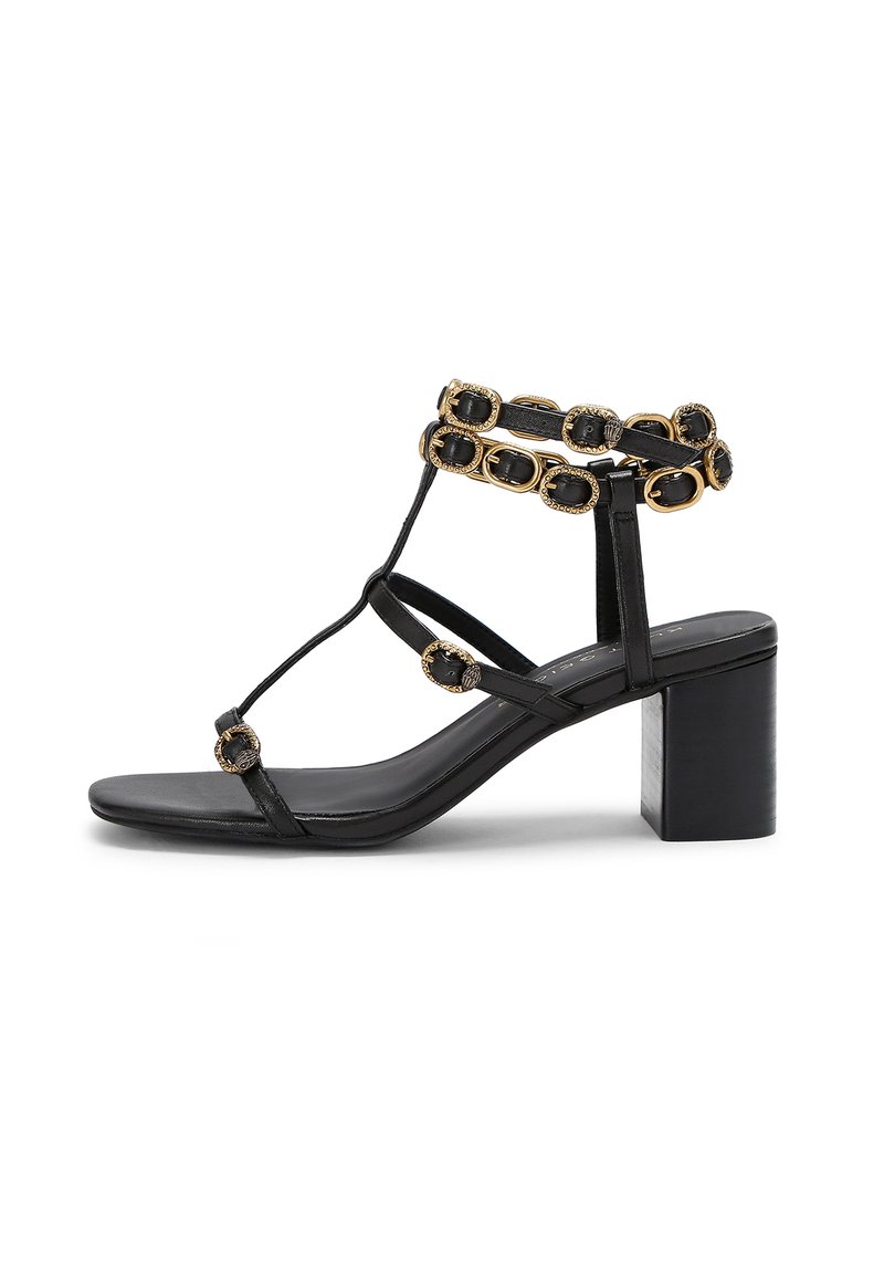 Czarne skórzane sandały z paskiem wokół kostki, z złotymi akcentami i dekoracyjnymi elementami, osadzone na grubym słupku.
