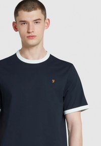 T-shirt in cotone navy con maniche corte, colletto e accenti sulle maniche a costine bianche, con un logo arancione sulla parte sinistra del petto.