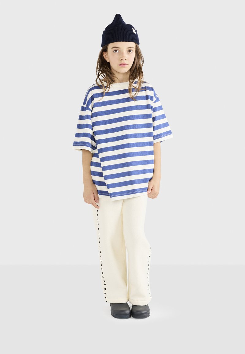 Blå og hvidstribet oversized t-shirt parret med cremede bukser med sort syninger ned ad siderne og sorte sko.