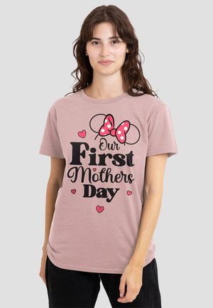 Woman with wavy brown hair wears pink shirt reading "Our First Mothers Day" with Minnie Mouse ears and a red polka-dot bow, hearts around text.