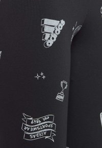 Leggings negras con gráficos en blanco, que incluyen logotipos y diseños de trofeos, con una textura suave y un diseño ajustado.