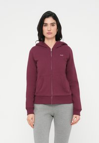 Μακρύ φούτερ με φερμουάρ σε βουργουνδί απόχρωση, με μπροστινή τσέπη, ριμπ μανσέτες και τελείωμα, και μικρή λεπτομέρεια λογότυπου στο αριστερό στήθος. Μαλακό ύφασμα από βαμβακερό μείγμα.