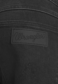 Černá denimová látka se šitým znakem značky Wrangler a charakteristickým prošíváním "W" na zadní kapse.