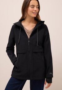 Zwarte softshell jas met een capuchon, koordjes, twee voorkeizen en een ritssluiting. Kenmerkt zich door een zachte textuur en subtiele branding.