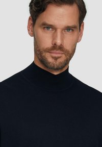 Marineblauer Strickpullover mit hohem Kragen und geripptem Muster. Figurbetontes Design mit glatter Oberfläche, das einen sauberen und minimalistischen Stil präsentiert.