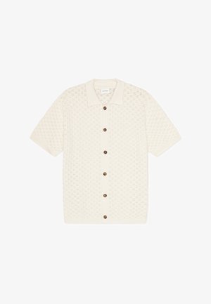 Pletena polo majica s kratkim rukavima u boji slonovače. Ima teksturu s uzorkom, pet smeđih dugmadi sprijeda i mekani ovratnik.