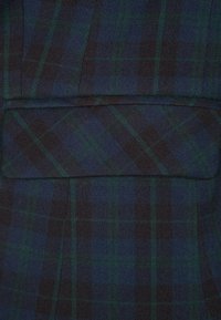 Tartan textilie s tmavě modrými, černými a zelenými vzory. Tkanina vypadá hladce s strukturovaným designem a plochými švy.