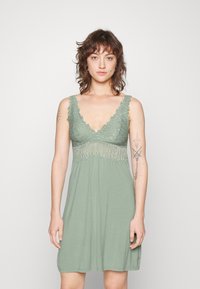 Hellgrünes Kleid mit tiefem V-Ausschnitt, Spitzenbesatz an der Brust und einem fließenden, lockeren Schnitt. Verfügt über verstellbare Träger und dekorative Nähte.