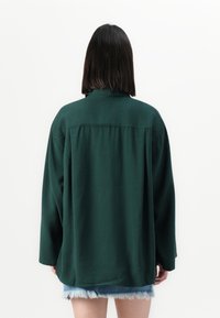 Mørkegrønn oversized skjorte med lange ermer, bakre yoke og myk tekstur, kombinert med lyseblå denimshorts med frayed hem.