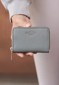 Portafogli in pelle grigia con chiusura a zip, caratterizzato da branding impresso e hardware in tono argento. Design compatto con dettagli di cucitura visibili.