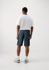 Marina cargo shorts med sidfickor, tillverkade av lättviktig textil. Matchas med en enfärgad vit t-shirt och sneakers i neutrala toner.