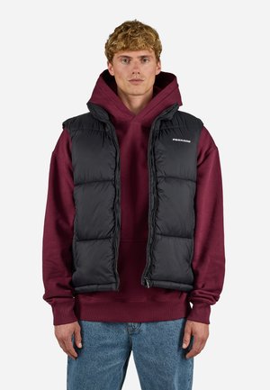 Black puffer vest with a zip front, padded design, and a slight sheen. Worn over a maroon hoodie, paired with blue jeans.