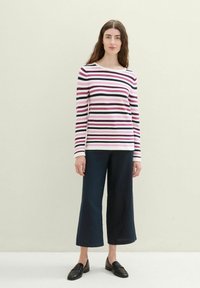 T-shirt à manches longues rayé rose, noir et blanc, associé à un pantalon large noir et des mocassins noirs. Design épuré et décontracté.