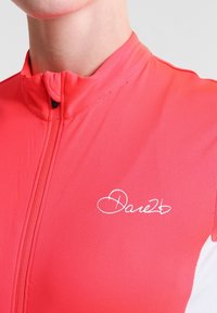 Czerwona, krótkorękawowa koszulka kolarska z teksturowanej, oddychającej tkaniny. Posiada wysoki kołnierz i biały logo na piersi. Zapięcie na zamek błyskawiczny z przodu.